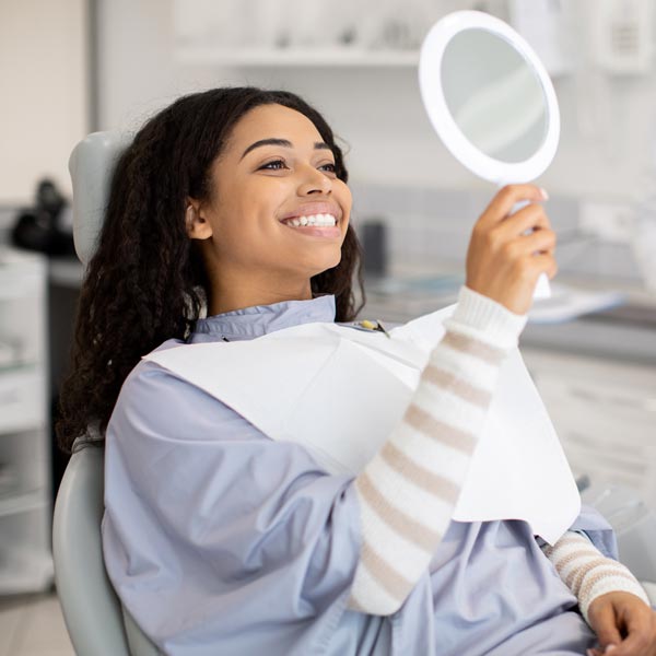 person smiling in hand mirror in dental chair