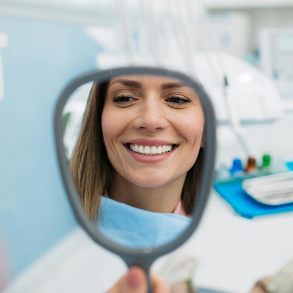 person smiling in hand mirror at dentist